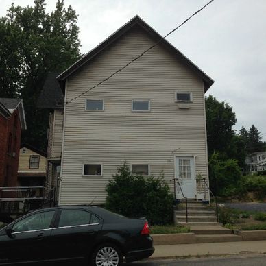 White two-story house with small windows and black car parked outside.