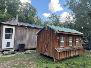 Two wooden sheds on a grassy yard under a partly cloudy sky.