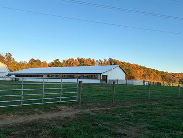 A white barn in a green field with autumn trees in the background under a clear blue sky.