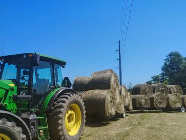 Green tractor with trailers loaded with hay bales under clear blue sky.