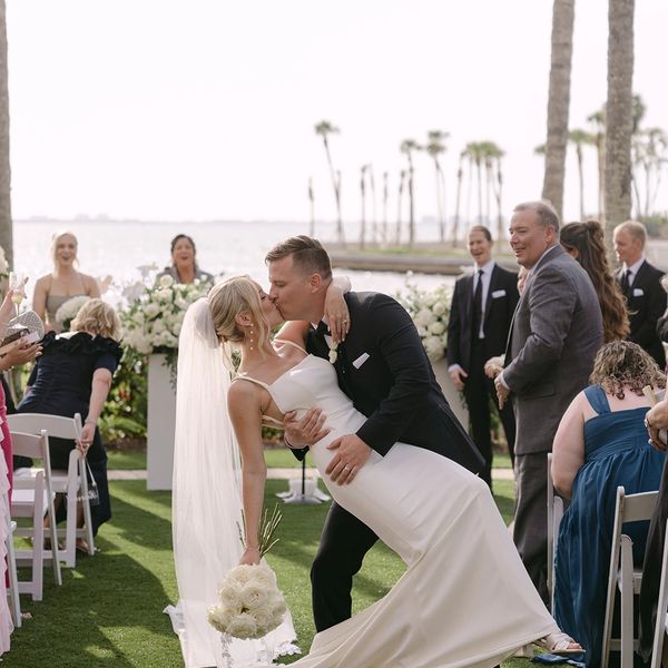 Bride and groom share a romantic dip and kiss at an outdoor wedding ceremony by the water.