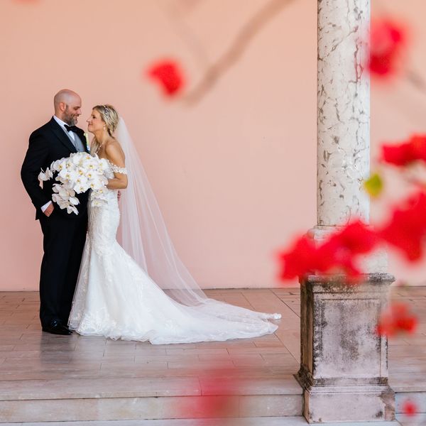 Bride and groom in elegant wedding attire posing with white orchid bouquet.