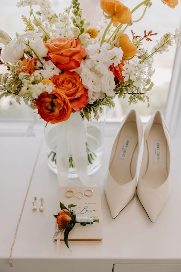 Elegant wedding accessories including shoes, floral bouquet, rings, and a boutonniere.
