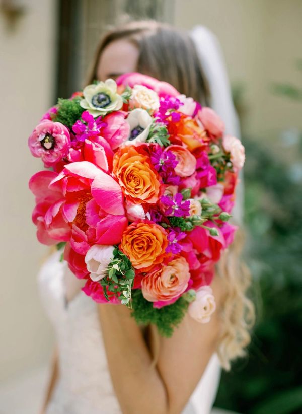 Bride holding a vibrant bouquet of mixed flowers, hiding her face.