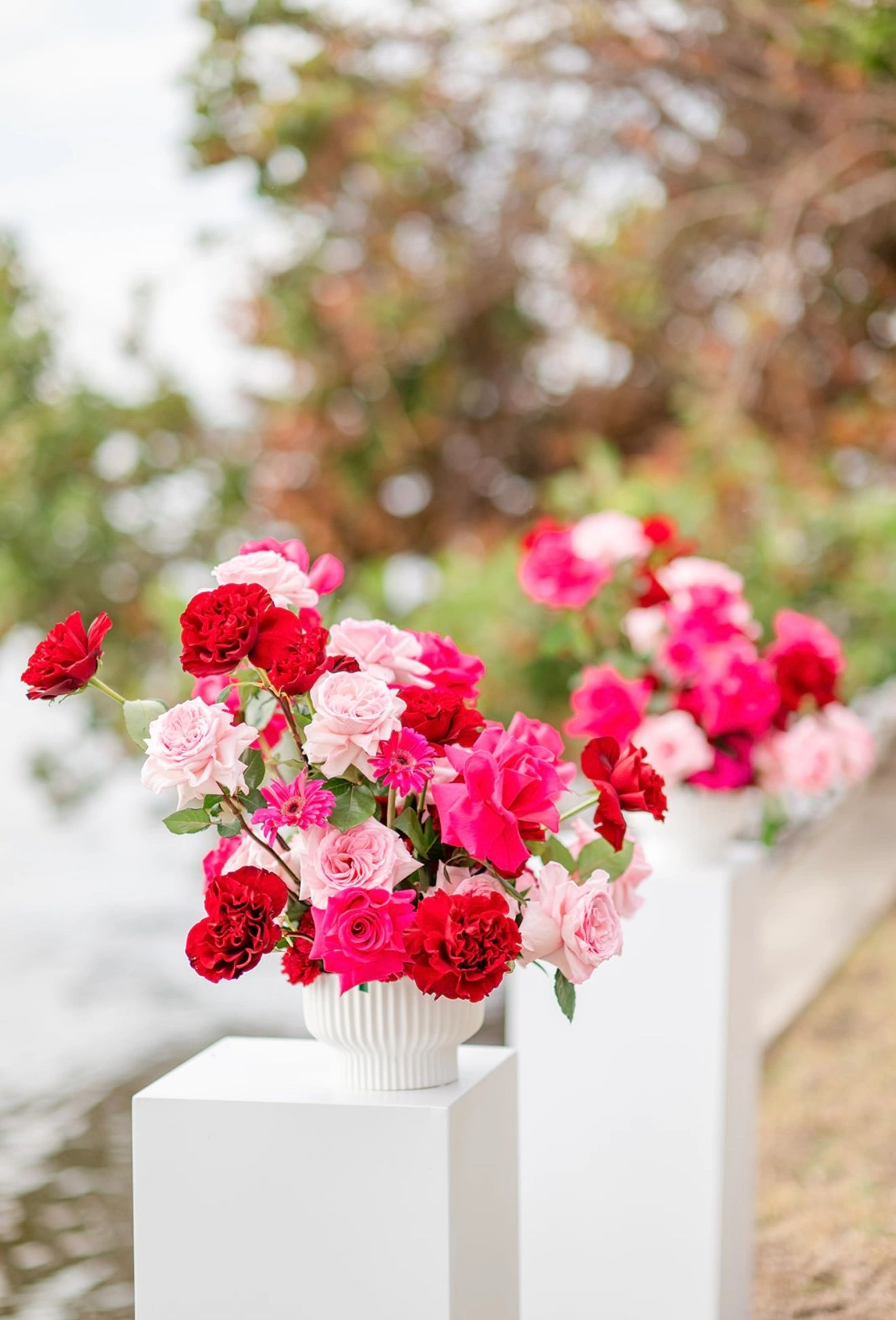 Vibrant red and pink floral arrangements in white vases on pedestals.