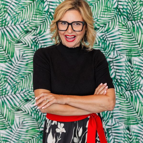 Cheerful woman with glasses posing confidently against a green leafy background.