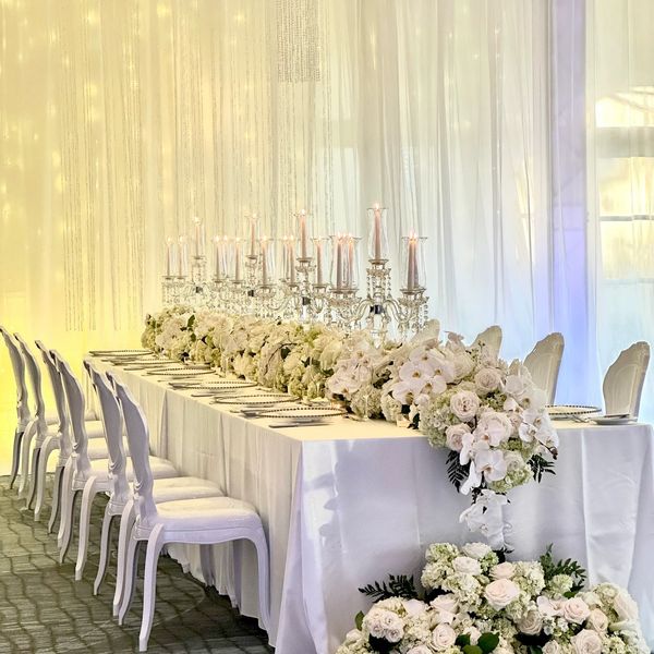 Elegant white floral centerpiece on a long banquet table with white chairs and candles.