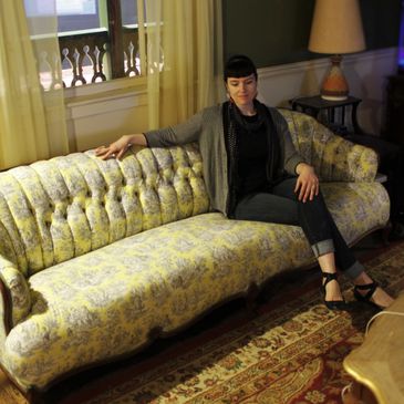 Heather sitting on the sofa she reupholstered for Meow Wolf's House of Eternal Return.