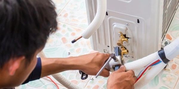Technician repairing a washing machine hose connection.