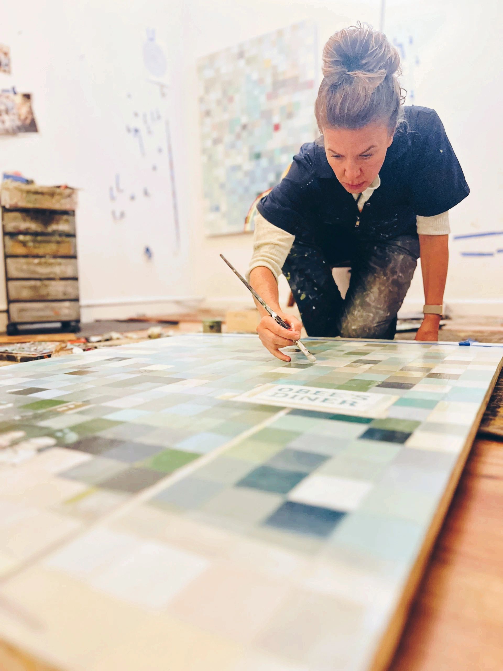Woman focused on painting a large mosaic artwork on the floor.