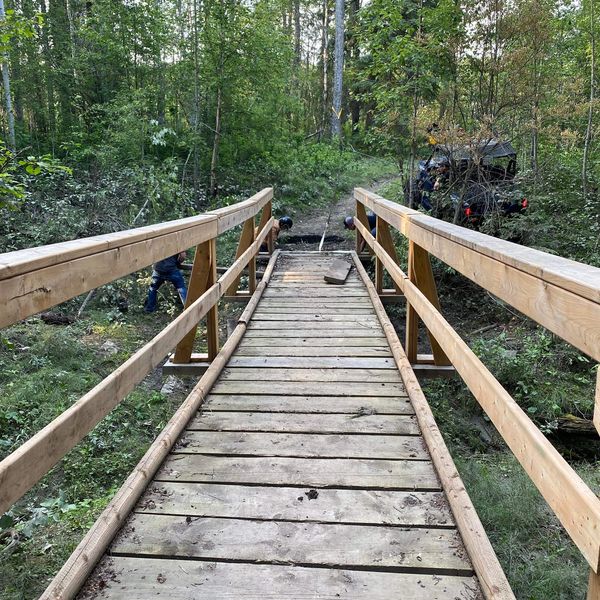 A wooden bridge in a forest with people and an ATV nearby.