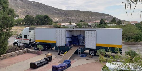 Moving truck with open doors unloading furniture on a driveway.