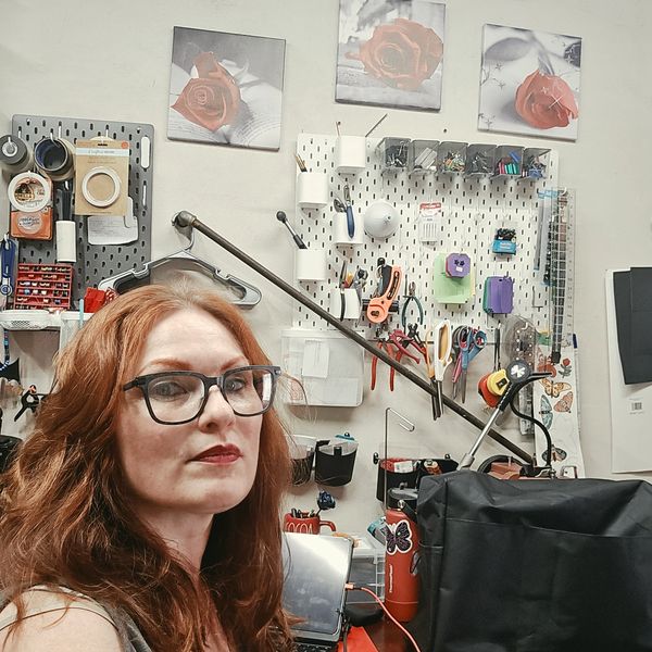 Woman with glasses in a workshop with tools on the wall.