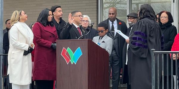 Man takes oath at a podium surrounded by people in formal attire.