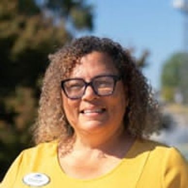 Smiling woman with glasses outdoors on a sunny day.