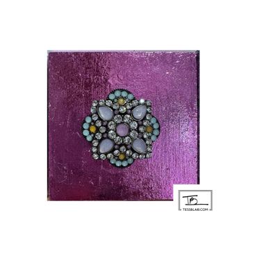 Vintage floral brooch with multicolored stones on a shiny purple background.