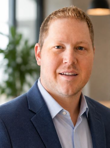Professional man in blue suit jacket and light blue shirt smiling indoors.