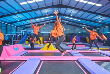 Group of people jumping on trampolines in a colorful indoor trampoline park.