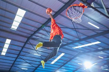 A basketball player in mid-air about to dunk the ball indoors.