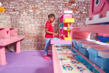 A child in a red shirt playing with a pink toy kitchen.