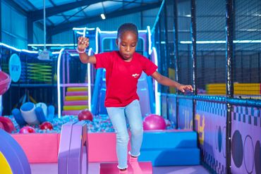 A girl in a red shirt balancing on soft play blocks at an indoor playground.