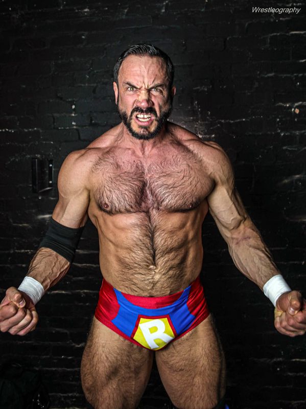 Muscular wrestler flexing fiercely in red and blue trunks with 'R' emblem.