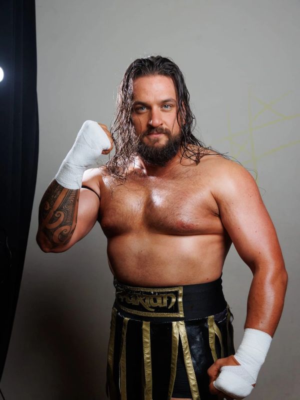 Muscular man with wrapped hands and long hair posing confidently.