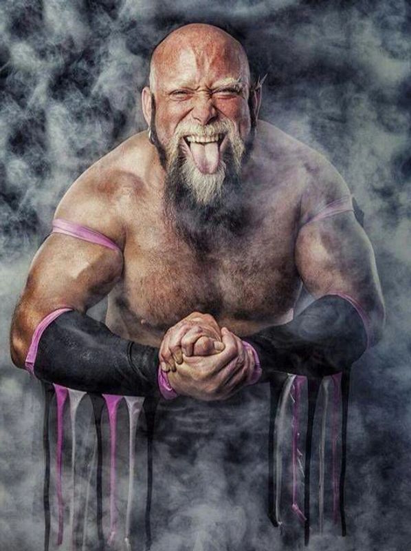 Muscular man with a beard sticks out his tongue surrounded by smoke.