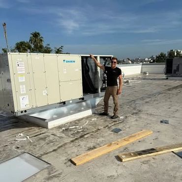 Man standing next to a large Daikin HVAC unit on a rooftop under a clear sky.