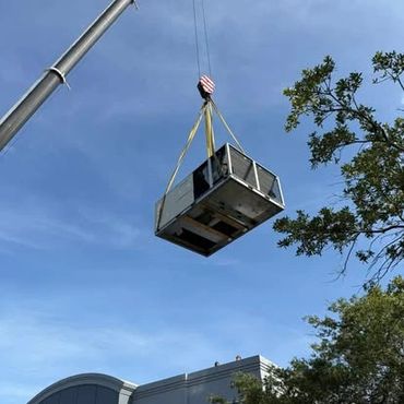 A crane lifts a large HVAC unit above a building.