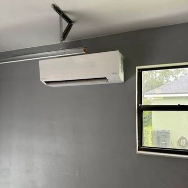 Wall-mounted air conditioner unit in a gray room next to a window.
