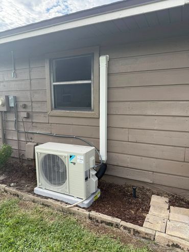 Outdoor HVAC unit installed next to a house wall with a small window.
