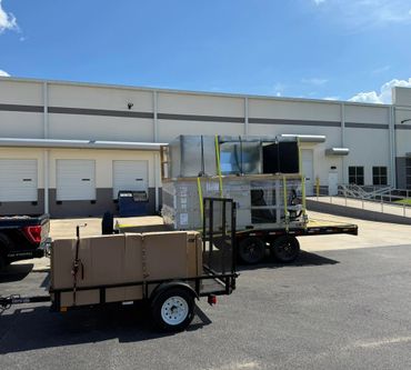 Two trailers loaded with industrial equipment parked outside a warehouse under clear sky.
