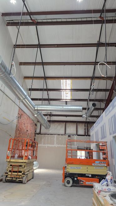 Interior of a construction site with ductwork and scissor lifts.