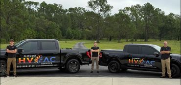 Three men stand confidently next to two black Clermont HVAC service trucks.