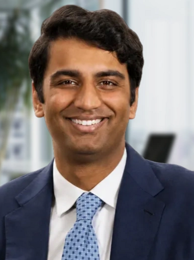 Smiling man in a blue suit and patterned tie.