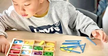 Child playing with colorful numbers and sticks at a table.