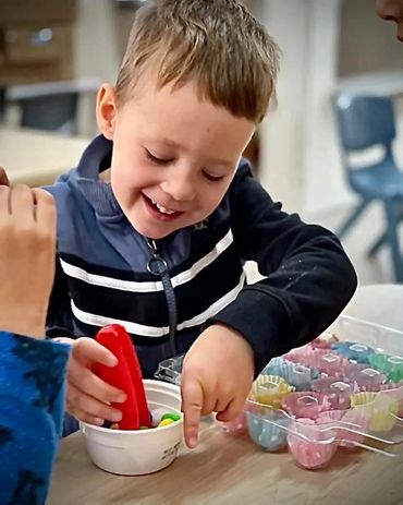 Young boy happily playing with colorful toys at a table.