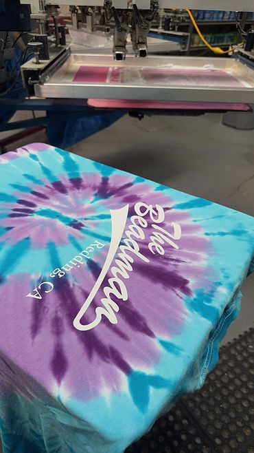 Colorful tie-dye shirt being screen printed with white text.