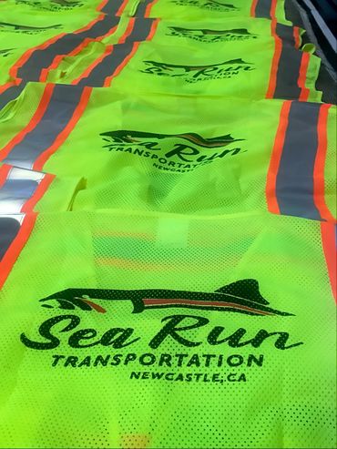Bright yellow safety vests with 'Sea Run Transportation' logo laid out in a row.