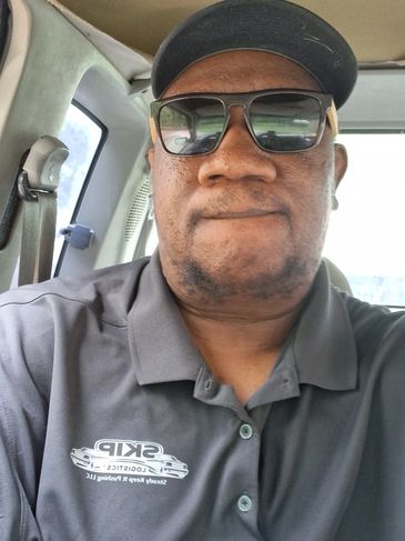 Man wearing sunglasses and a SKIP Logistics polo inside a vehicle.