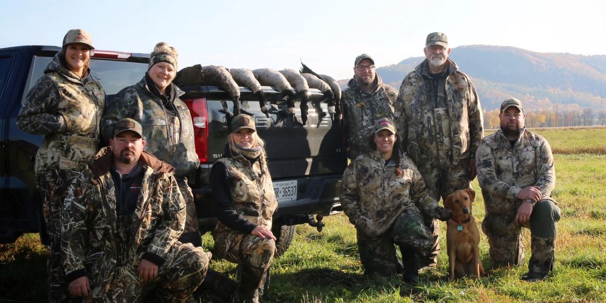 Group of hunters posing with their catch and a dog in a field.