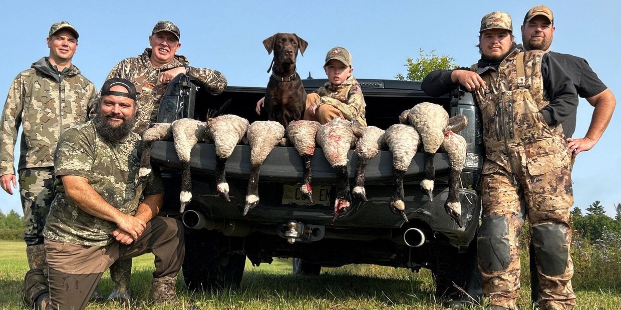 A group of hunters with their dog and hunted birds displayed on a truck tailgate.