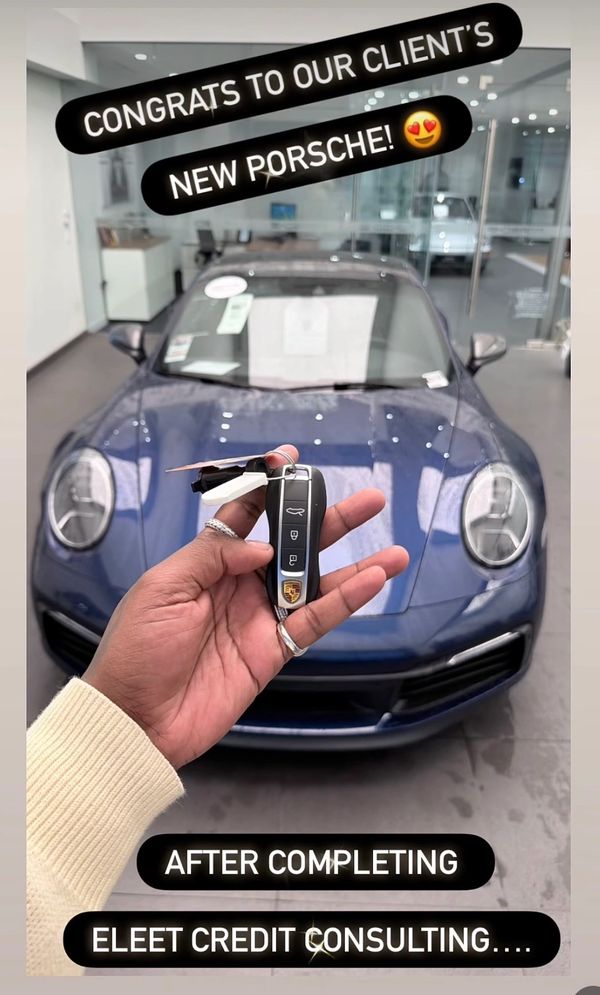 Hand holding Porsche car keys in front of a blue Porsche sports car inside a showroom.