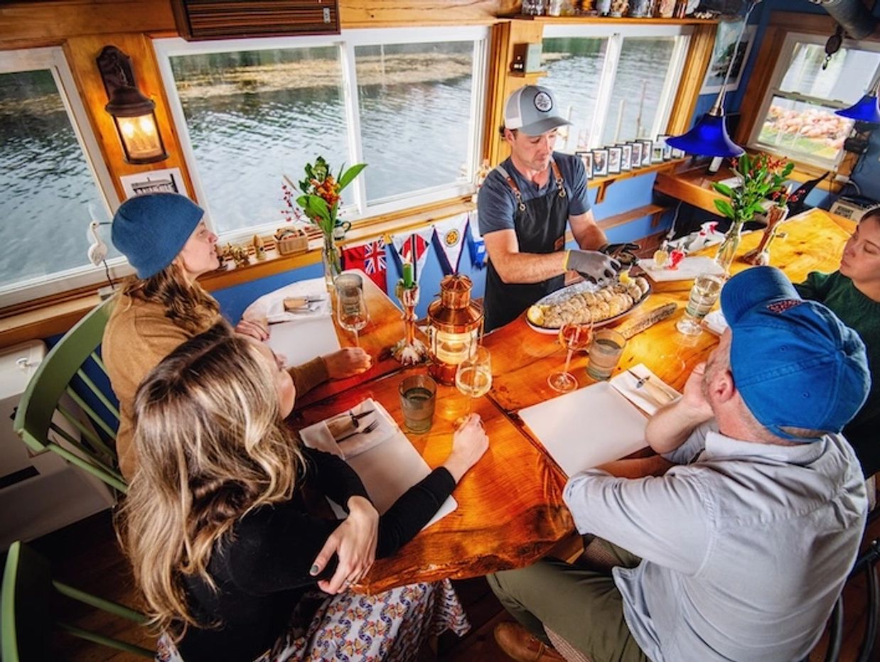 A group sitting by the water learning how to shuck oysters in Phippsburg Maine