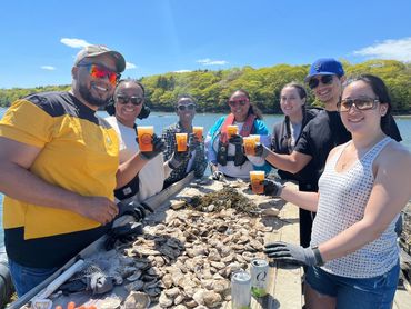 A group of people with cocktails in their hands toasting around a table covered with oysters.