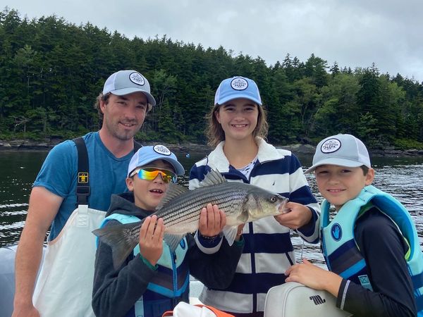 Captain Joe with 3 kids holding up a striper on a family fishing charter in Maine
