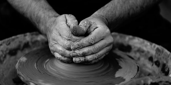Hands shaping clay on a pottery wheel in black and white.