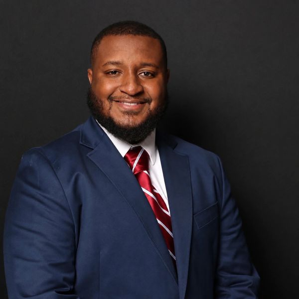 Smiling man in a blue suit and red-striped tie against a black background.