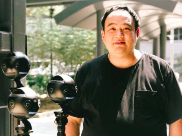 Man posing with 360-degree cameras outdoors.